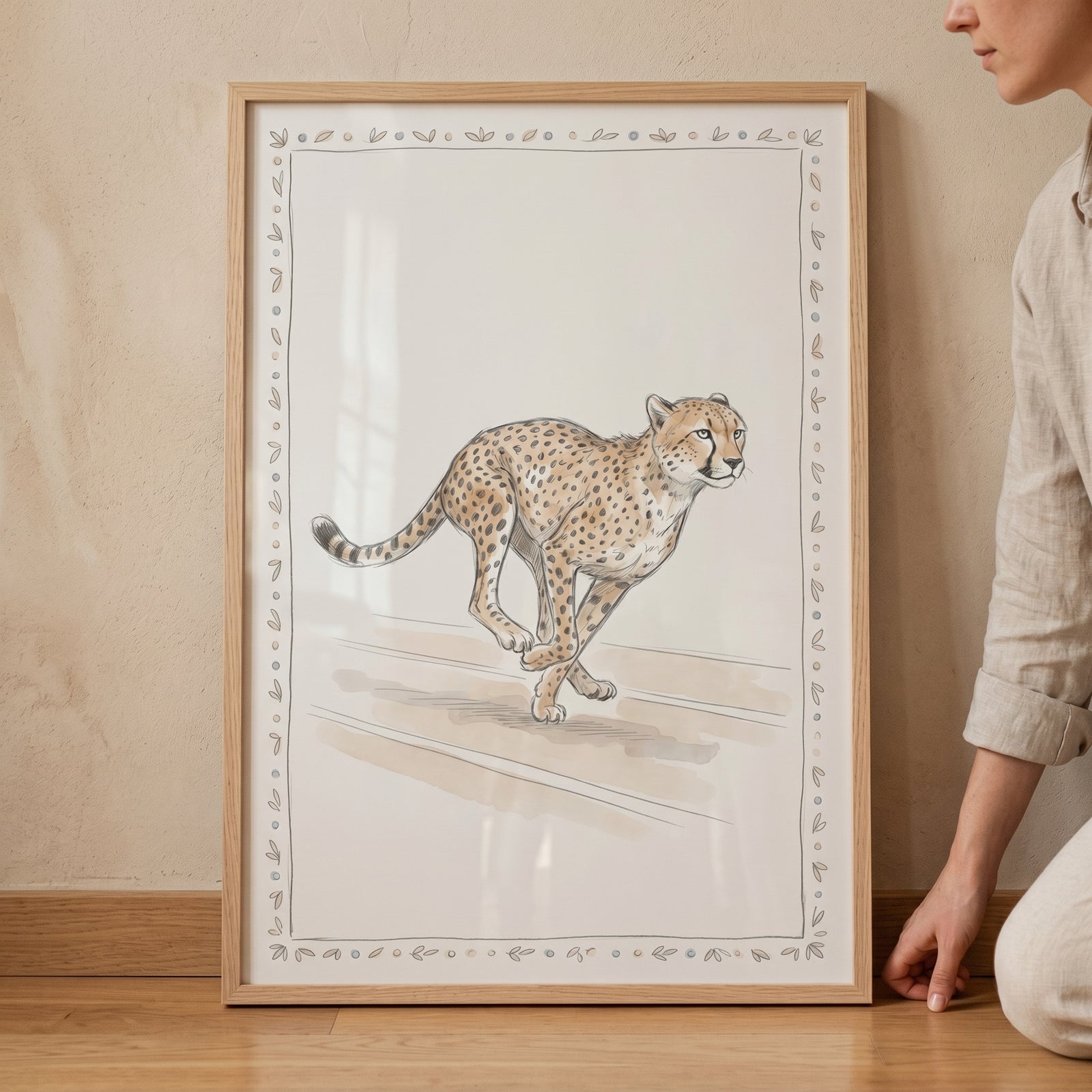 Neutral running cheetah artwork in a light wooden frame leaning against a wall next to a person.