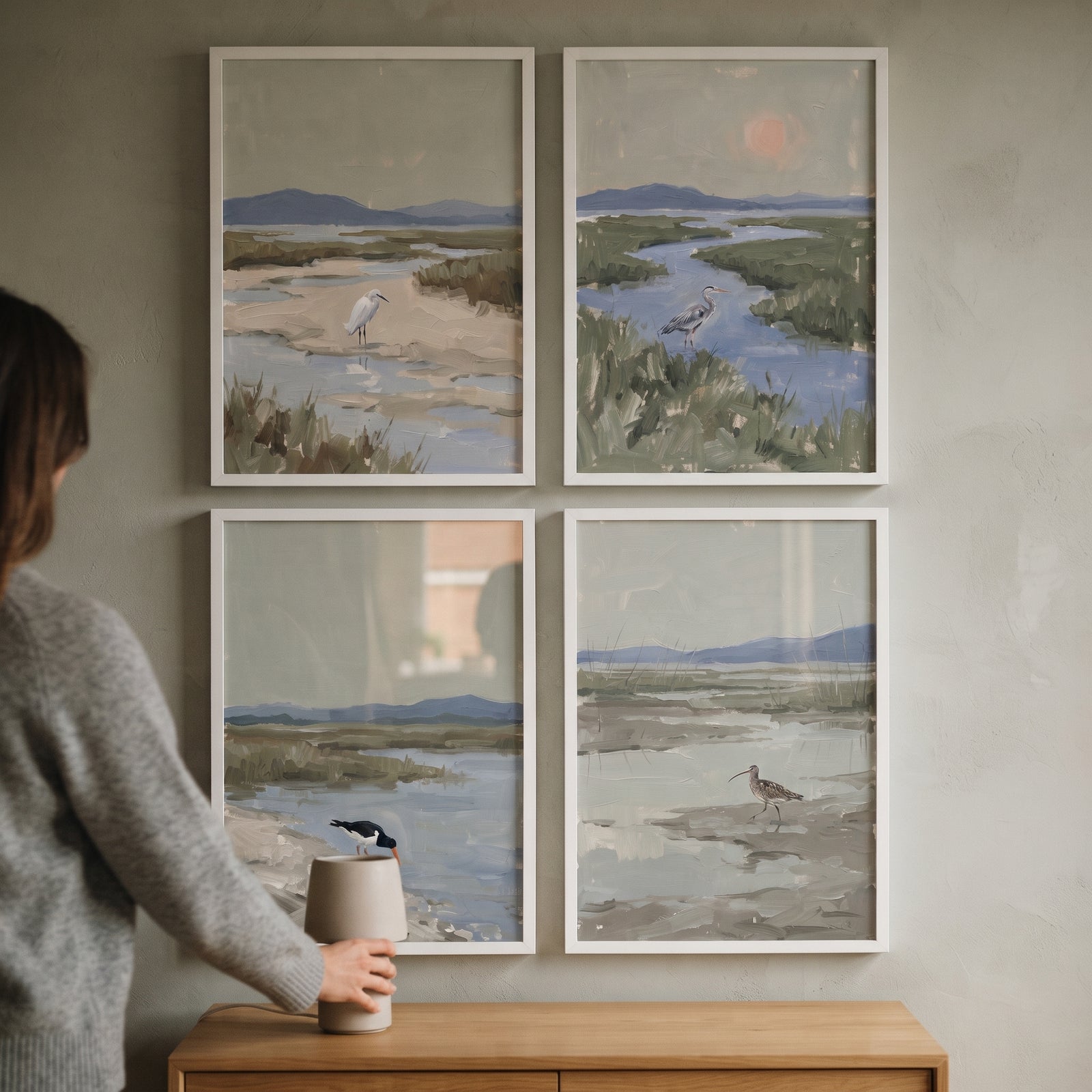 A person adjusts a lamp on a wooden sideboard below a neutral sage coastal bird wall art set of 4 in white frames.