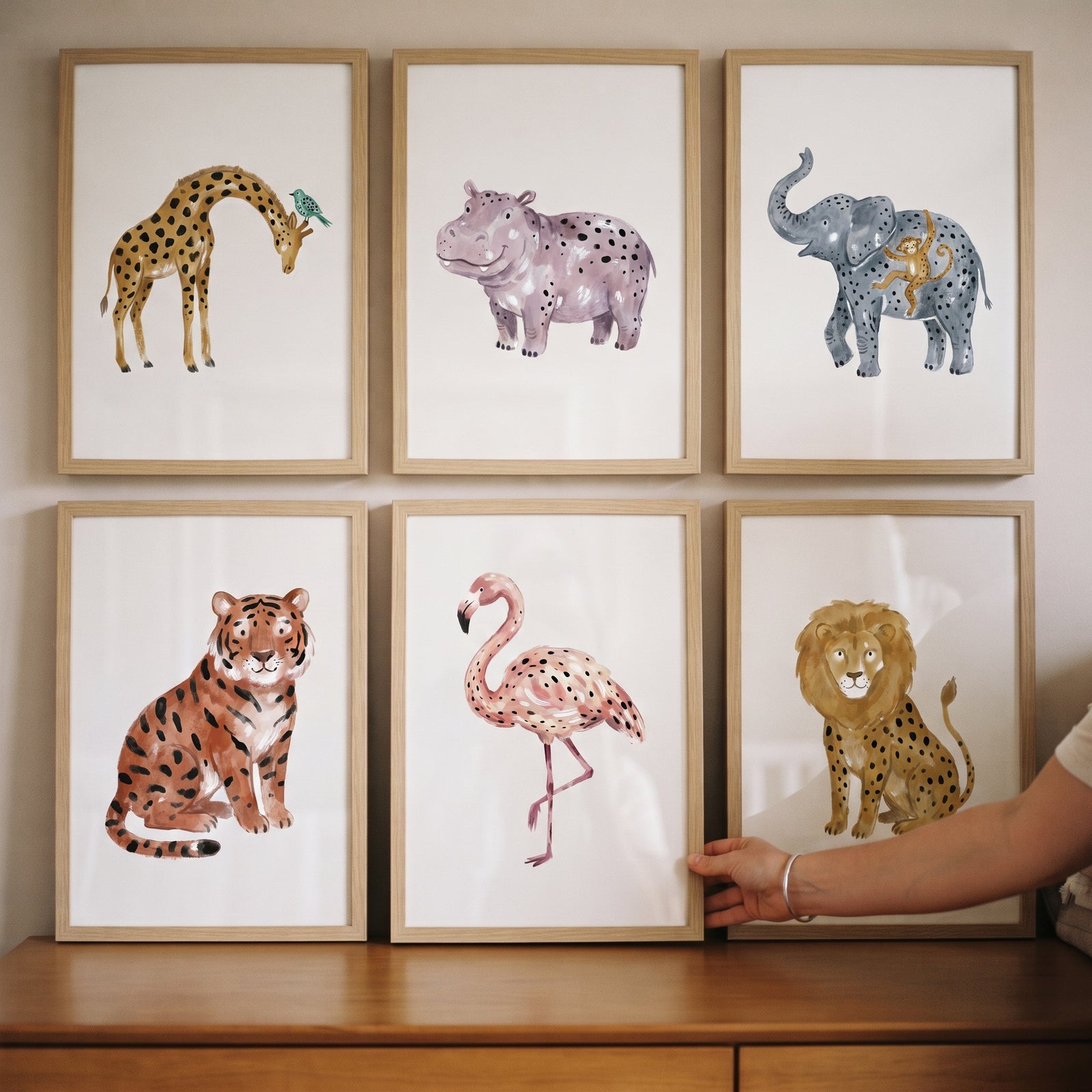 Neutral spotted safari animals wall art set of 6 watercolor prints in wooden frames displayed above a dresser.