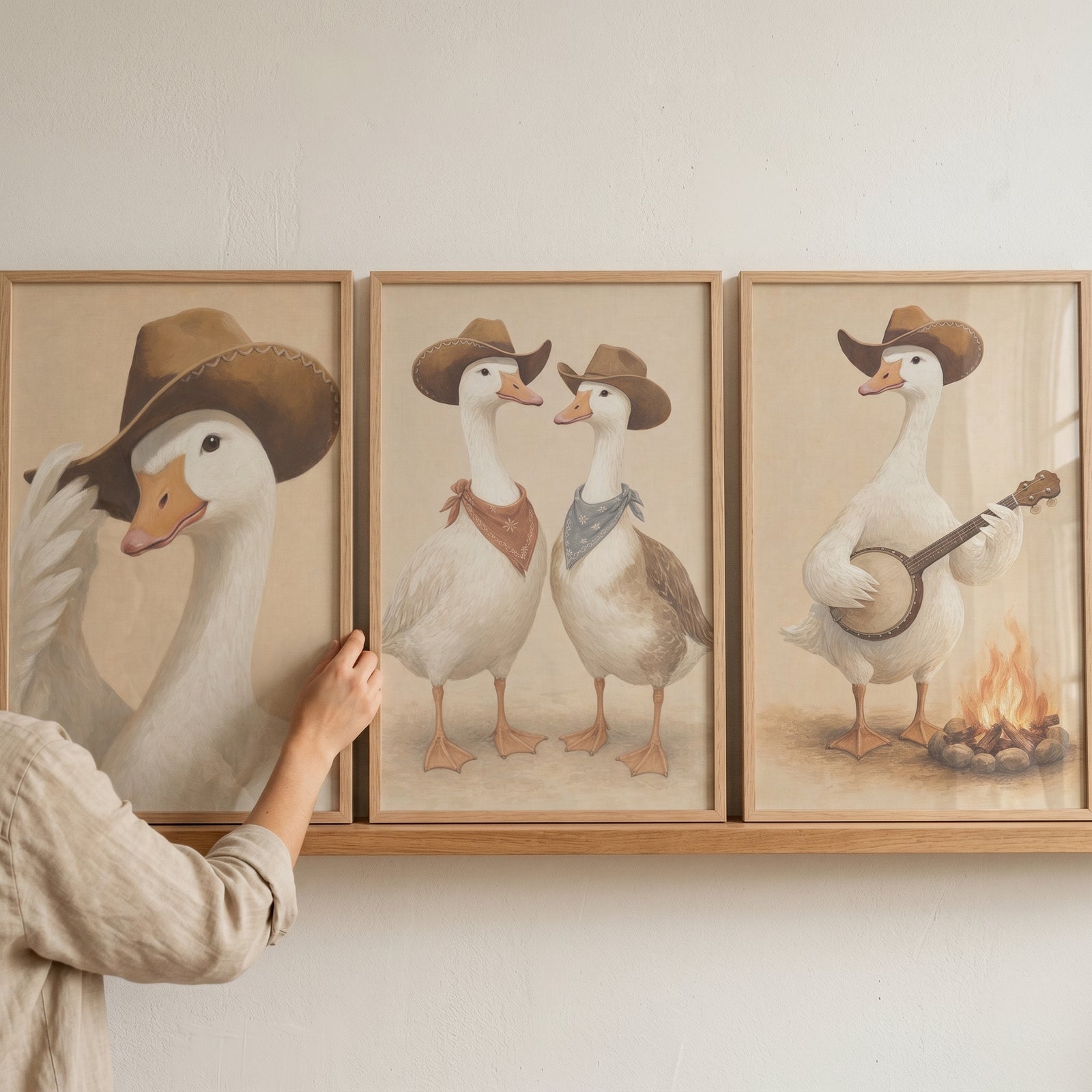 Neutral tan cowboy goose wall art set of 3 shows geese in hats playing banjo and wearing bandanas on a wooden shelf.