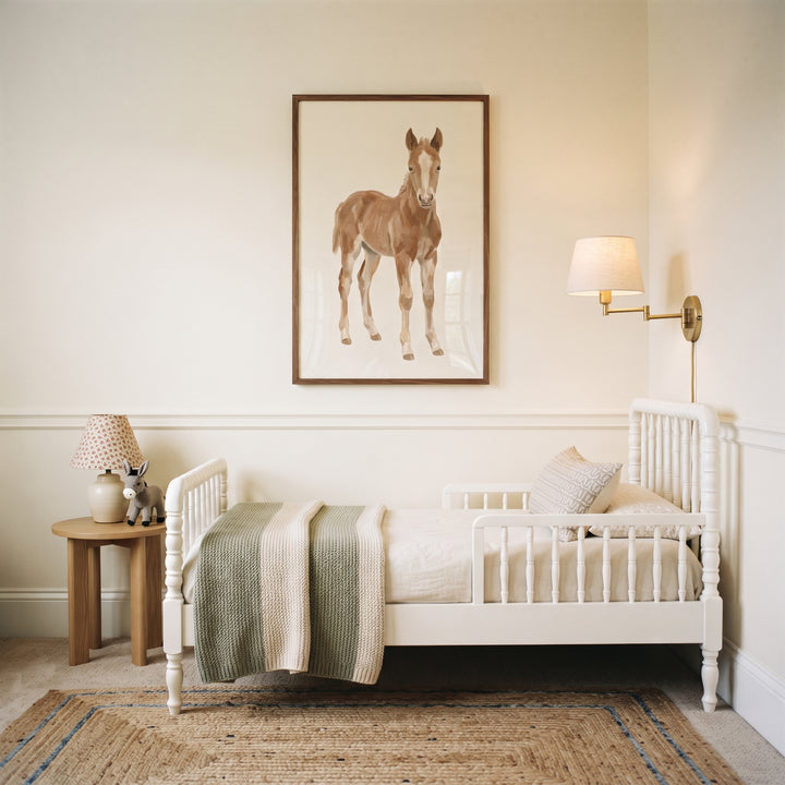 Neutral tan standing horse wall art hangs above a white spindle toddler bed in a cream-toned room with a jute rug.