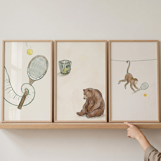 Neutral tennis animals wall art set of 3 features an elephant, bear, and monkey playing tennis on a wooden shelf.