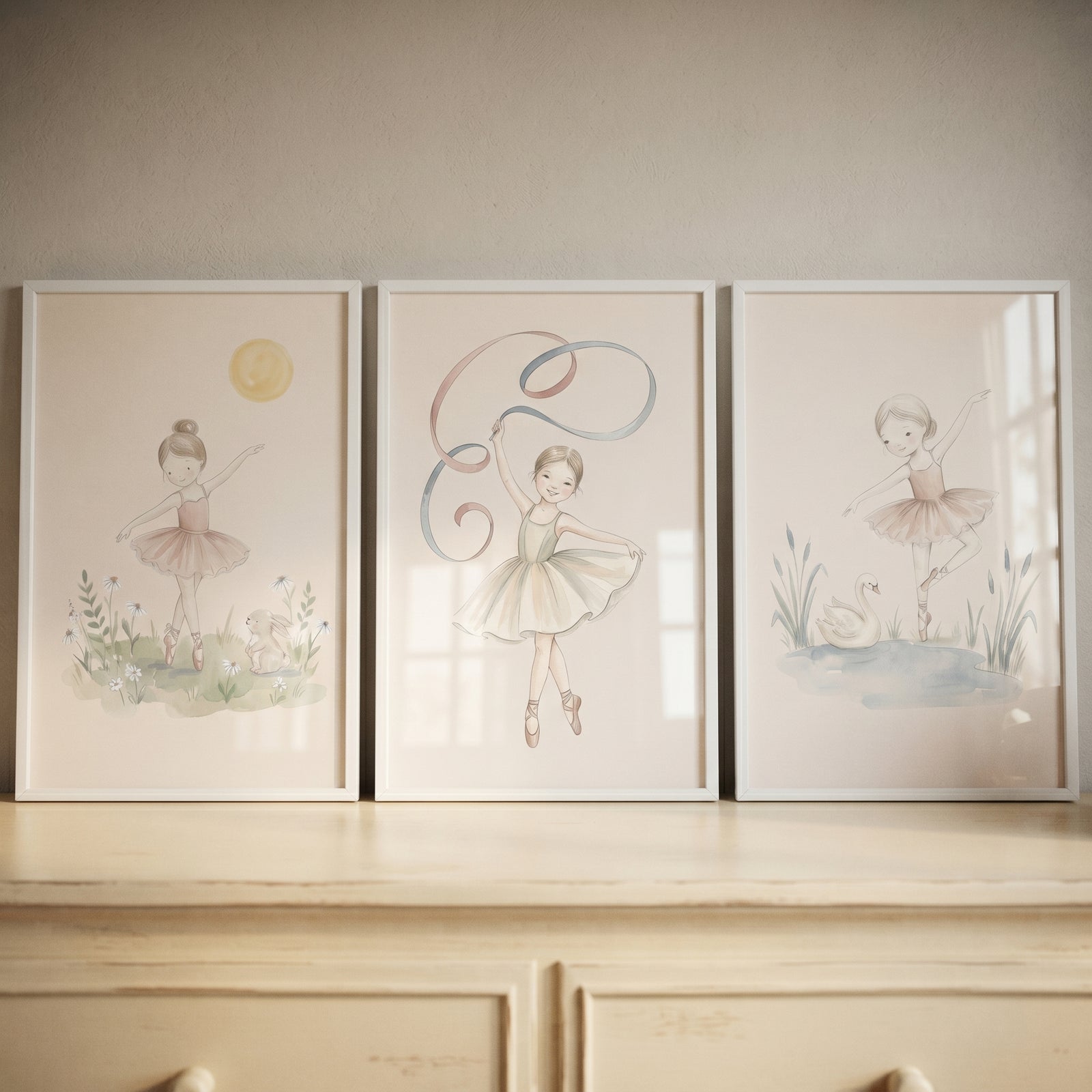 Neutral tone watercolor ballerina wall art set of 3 depicts dancers with a bunny, ribbon, and swan in white frames.