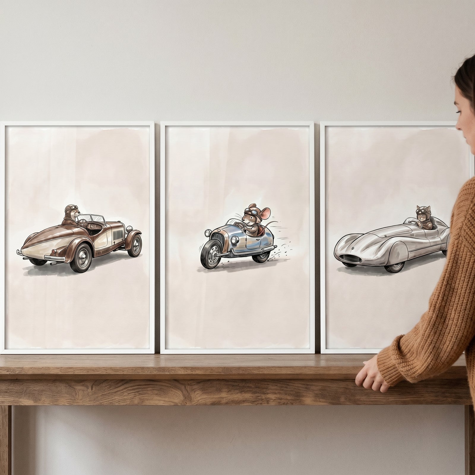 A person adjusts a neutral vintage driving animal wall art set of 3 featuring mice in classic cars on a wooden table.
