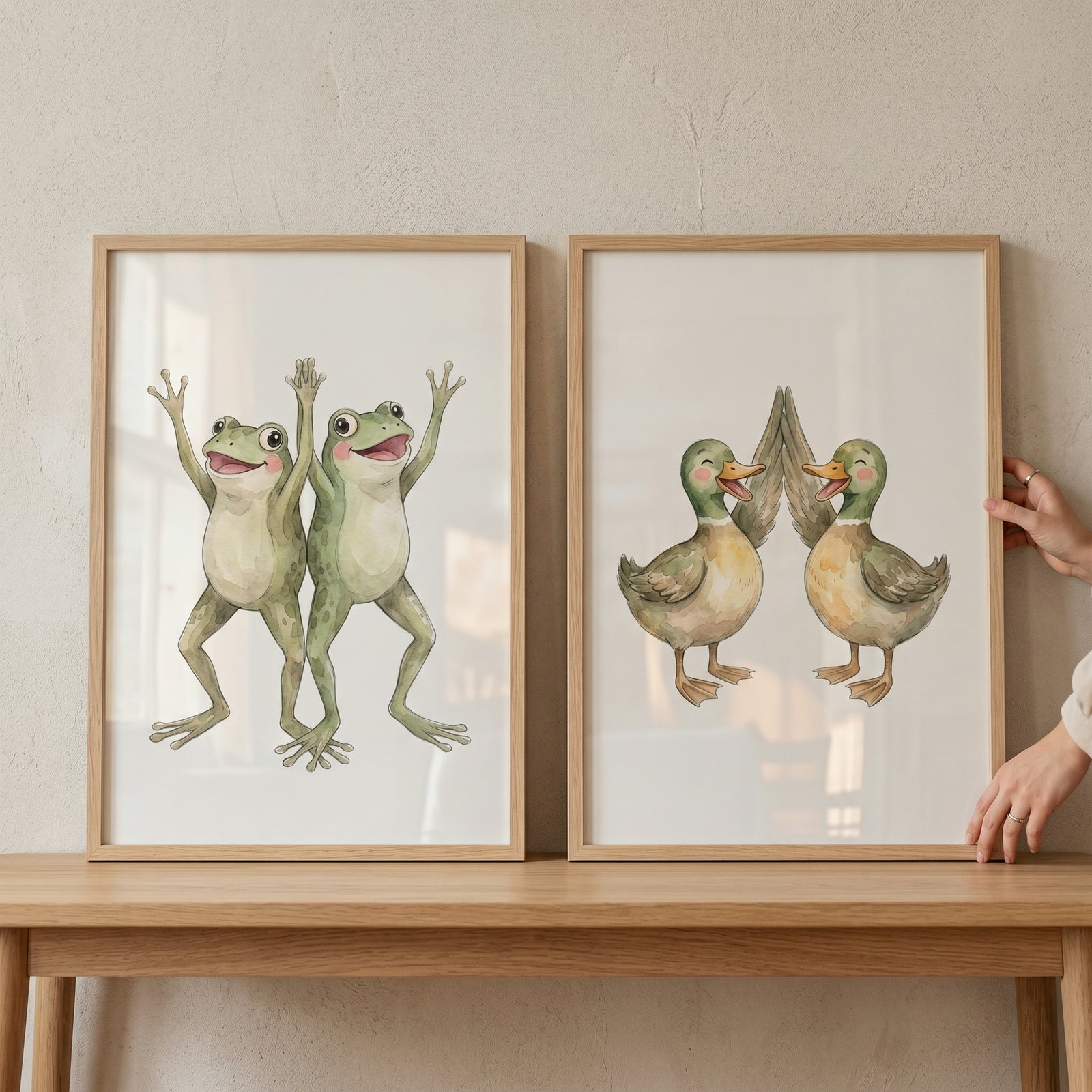 Neutral watercolor animal pair wall art set of 2 featuring smiling frogs and ducks high-fiving in light wood frames.