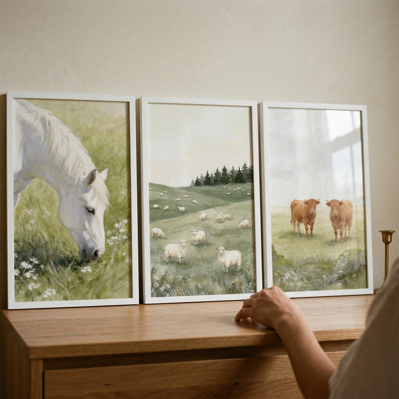 Neutral watercolor farm animal wall art set of 3 featuring horse, sheep, and cows on a wooden dresser with a hand.