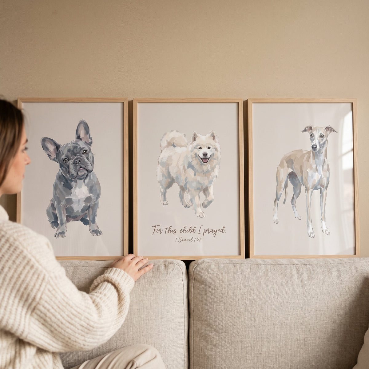 A woman views a neutral watercolor pet dogs wall art set of 3 featuring a French bulldog, Samoyed, and greyhound.