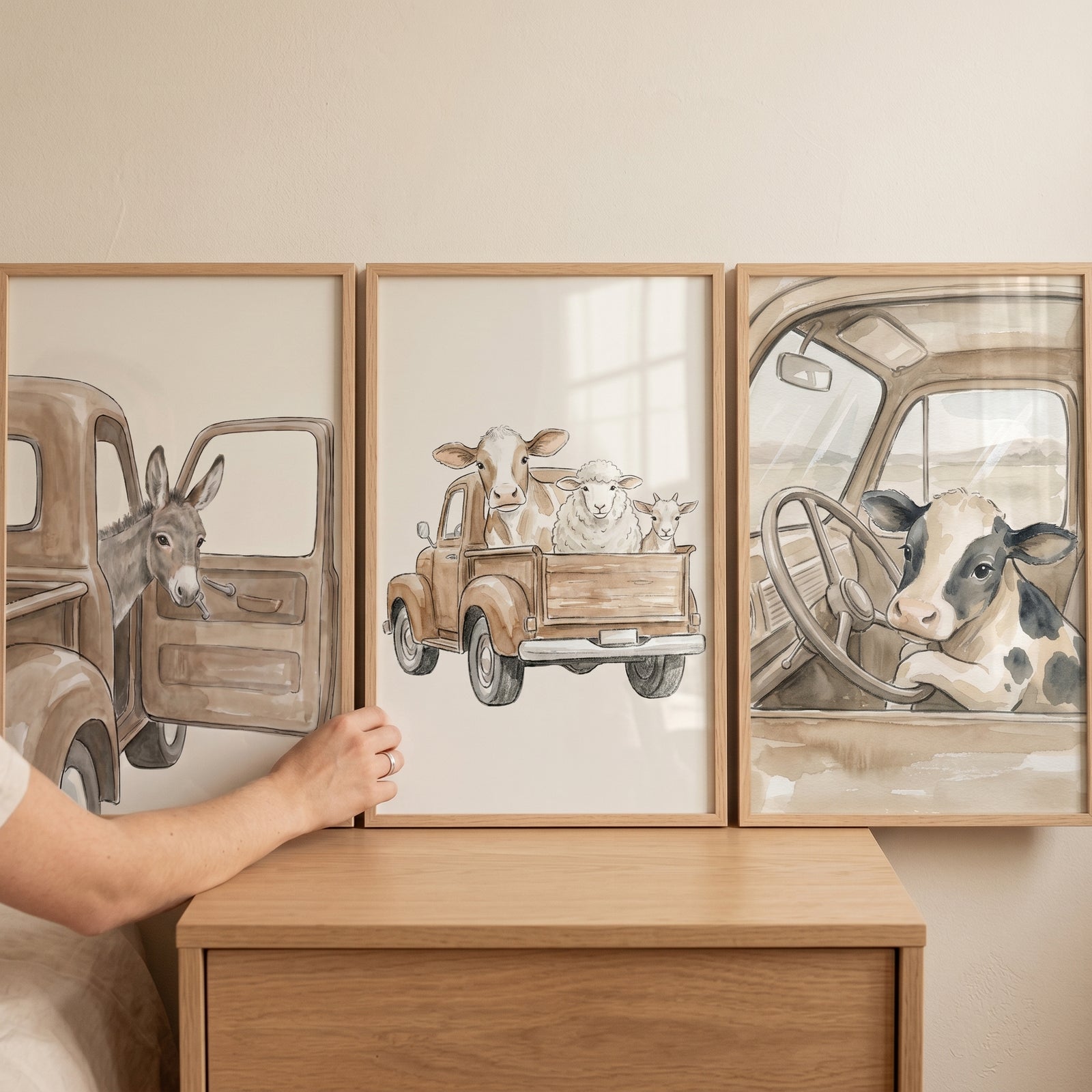 Hand adjusting a neutral watercolor truck animals wall art set of 3 featuring farm animals sitting in vintage trucks.