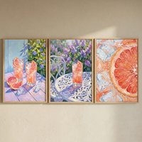 A triptych of framed wall art hangs on a neutral surface, capturing a sun-drenched garden setting. In the first piece, two glasses of pink citrus drink and ice cubes sit on a lavender table with fruit wedges. The middle work features a single glass on a white metal table surrounded by purple blossoms. The final piece provides a detailed close-up of a citrus slice and ice in a bubbly liquid. The style is textural and colorful, with an emphasis on light and shadow.