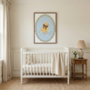 A peaceful and elegant nursery features a white wooden spindle-style crib positioned against an off-white wall with traditional molding. Inside the crib sits a soft plush lamb, and a cream-colored textile is draped over one side. Centered above the crib is a dark wood frame containing a charming illustration of a yellow duckling adorned with a brown bow. The duckling is surrounded by tiny white flowers on a light blue oval background, bordered by a decorative scalloped pattern in sage green.