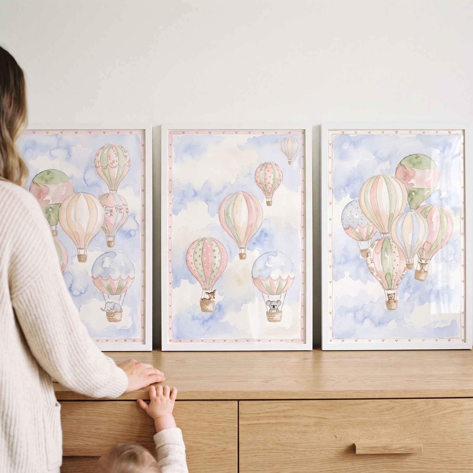 Watercolor nursery hot air balloon wall art set of 3 featuring cute animals sits on a wooden dresser.