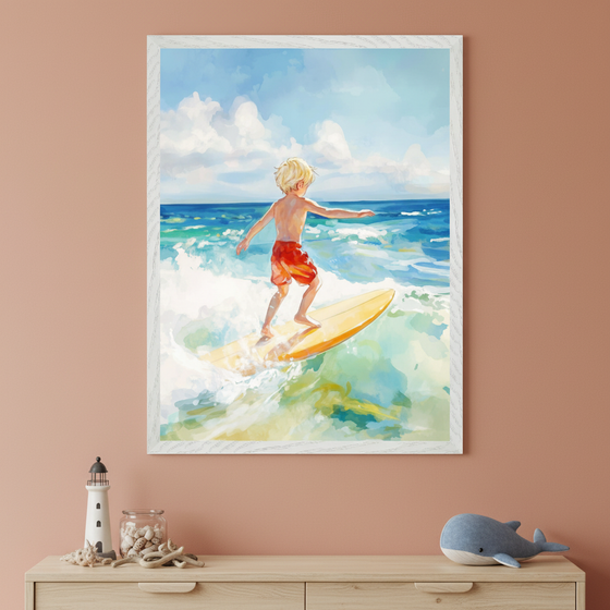 Framed watercolor-style artwork of a young blonde child in red swim trunks surfing on a yellow board, riding a wave under a bright blue sky with fluffy white clouds. The painting hangs on a peach-colored wall above a wooden dresser decorated with a lighthouse figurine, seashells, and a plush whale.