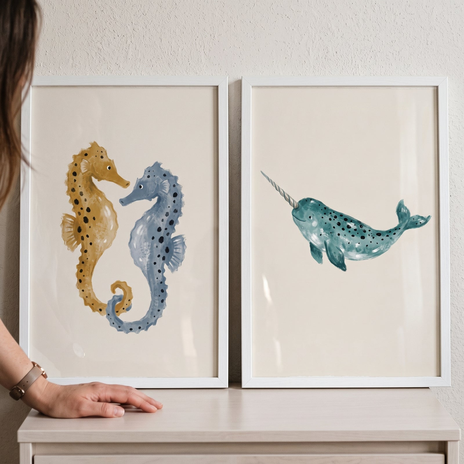 Ochre blue sea animal wall art set of 2 features seahorses and a narwhal in white frames on a light wood surface.
