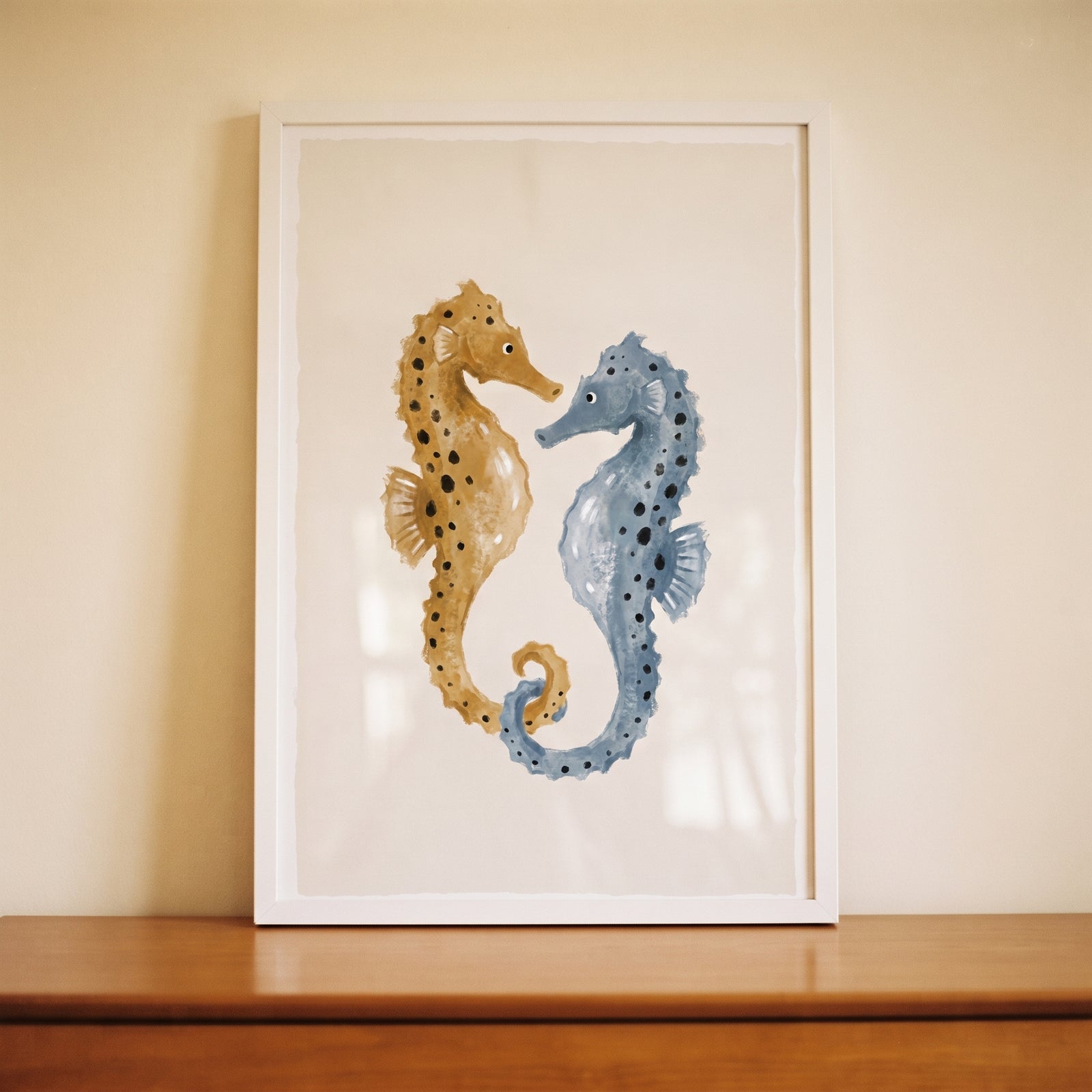 Ochre blue spotted seahorses wall art in a white frame, featuring two speckled sea creatures facing each other.
