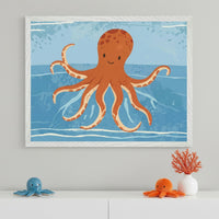 Modern kid's room with a white dresser. A large white-framed cartoon illustration of a smiling orange octopus swimming in blue water hangs centered above the dresser. On the dresser are a blue octopus plush, an orange octopus plush, and orange coral in a white vase.