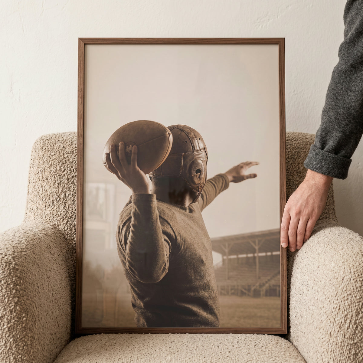 Framed old leather helmet quarterback sports wall art held by a person on a textured armchair.