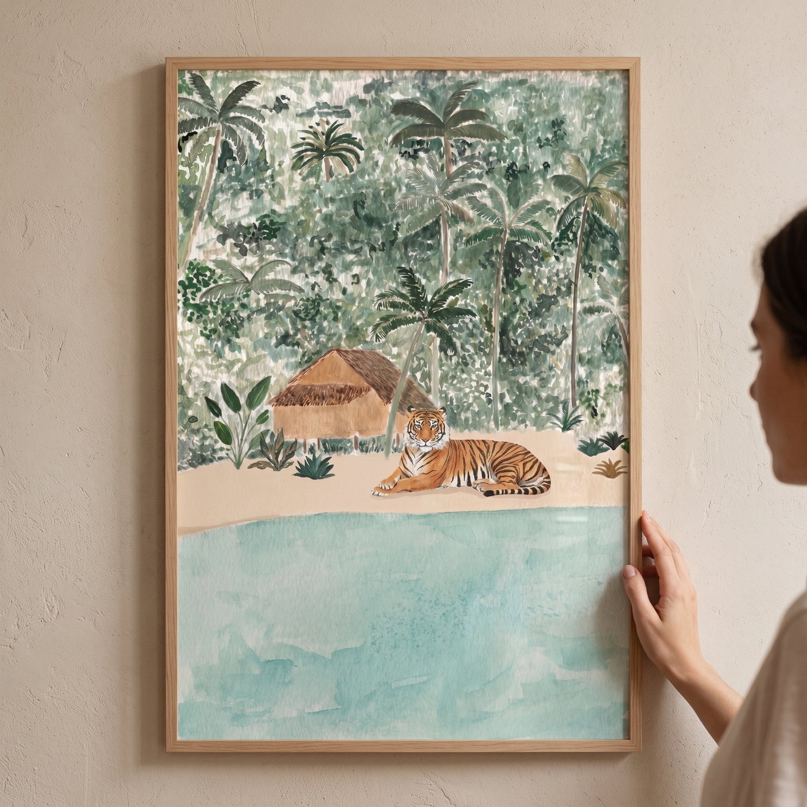 Orange striped tiger wall art depicts a tiger resting on a beach with a hut and jungle, held in a light wood frame.