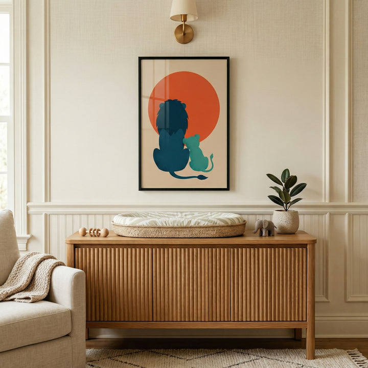 Framed lion and cub illustration centered above a wooden cabinet in a softly lit nursery with neutral decor and a changing pad on top. The warm red sun behind the figures draws attention to the artwork as a calming focal point in the space.