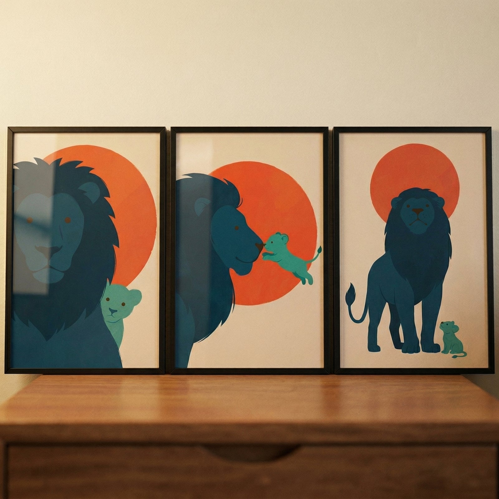 Three vertical black-framed minimalist illustrations are displayed in a row atop a wooden chest of drawers. Each piece features a large, dark blue lion and a small turquoise lion cub against a light beige background with a large orange circular sun. 