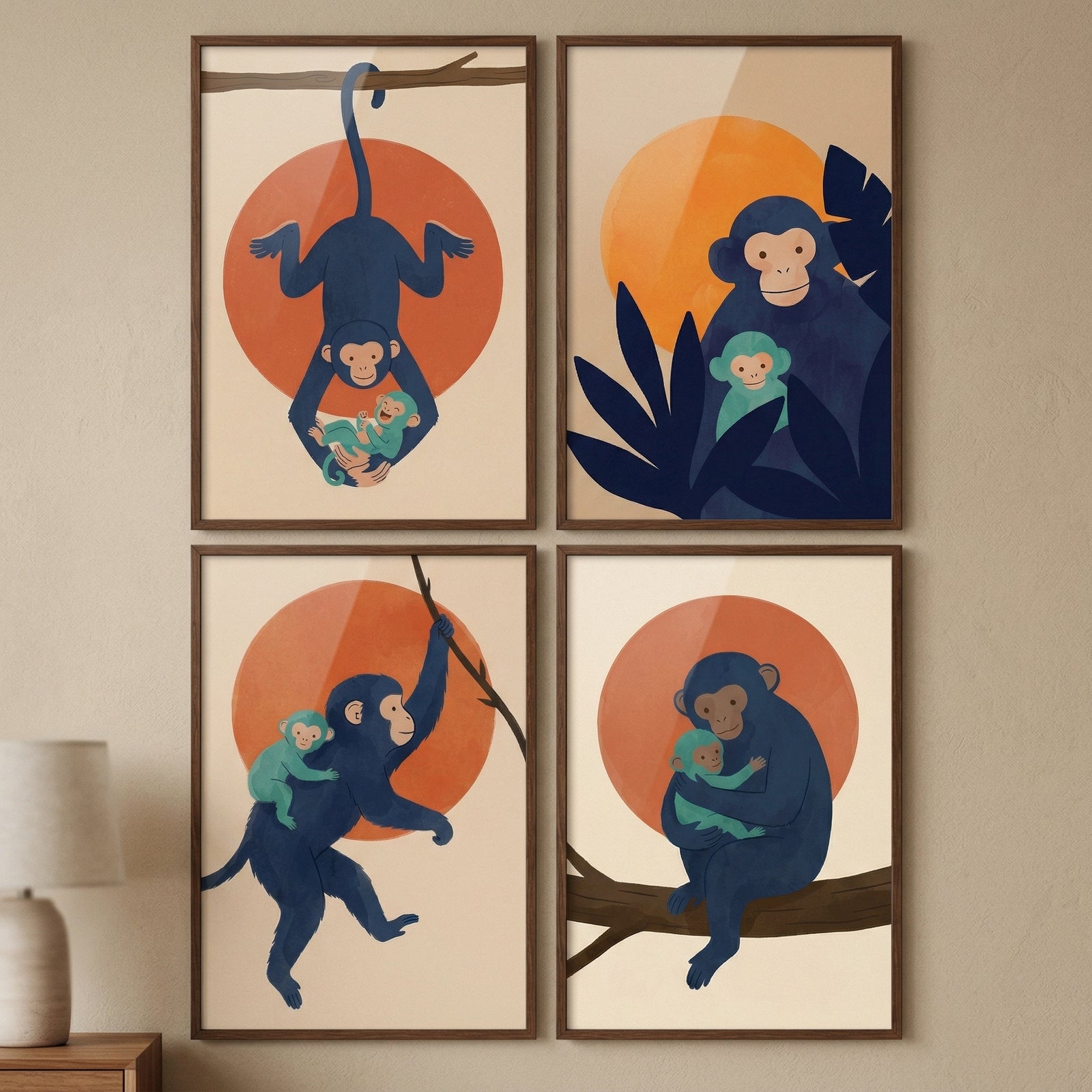 A set of four minimalist framed illustrations is displayed in a two-by-two grid on a beige wall. Each illustration features a stylized navy blue monkey and a small teal-colored infant monkey set against a cream background with a large orange sun-like circle.
