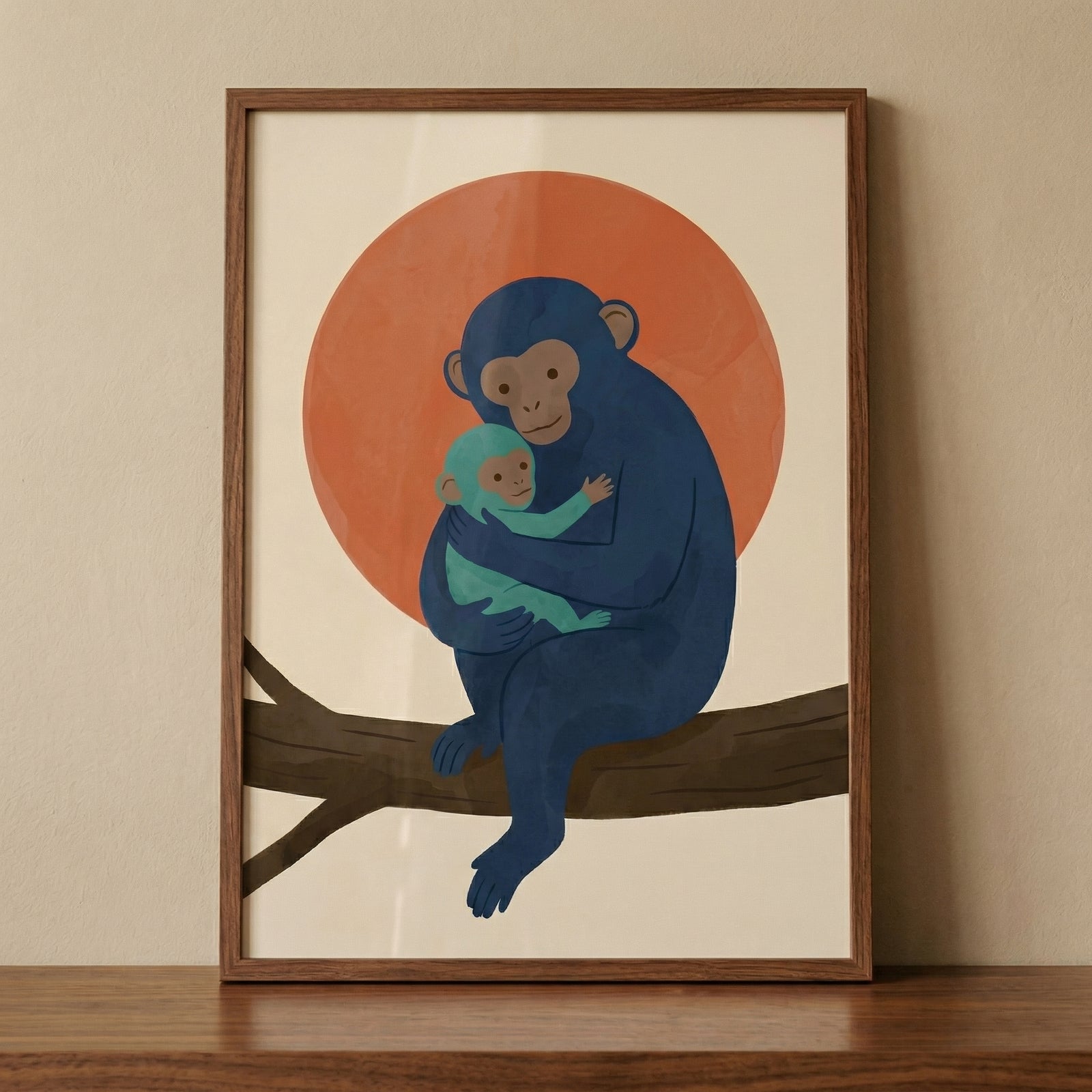 A minimalist framed illustration features an adult and a baby monkey. The larger monkey is colored in shades of blue and sits on a brown tree branch, cradling a smaller, light-teal baby monkey. Behind them is a large, solid orange circular shape, evoking a sunset or rising sun. The background of the print is a soft beige color. The artwork is housed in a simple, warm-toned wooden frame, which is resting on a dark wood surface against a neutral, off-white wall.