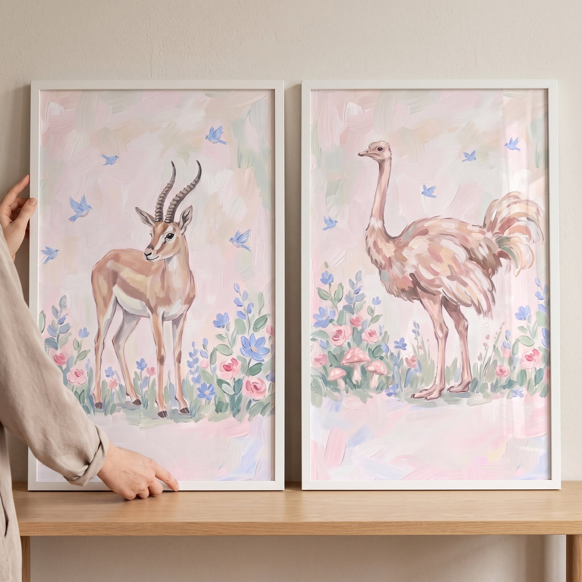 Hands hold a painterly floral safari animals wall art set of 2 featuring an antelope and an ostrich in pastel hues.