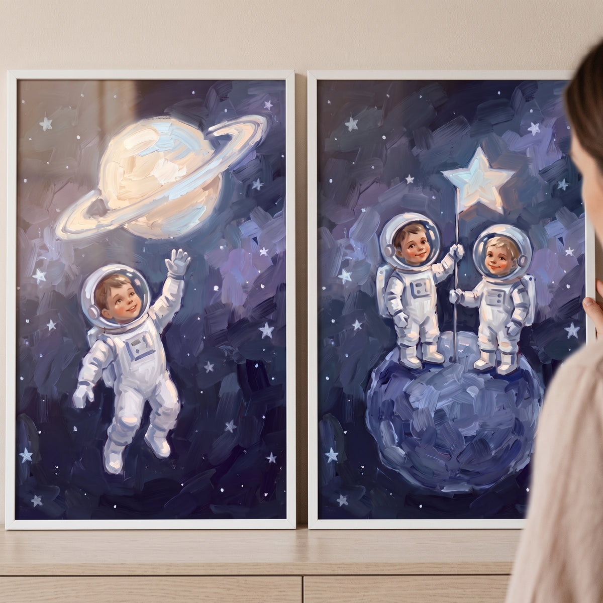 Painterly navy baby astronaut wall art set of 2 depicts children in spacesuits near a ringed planet and on the moon.