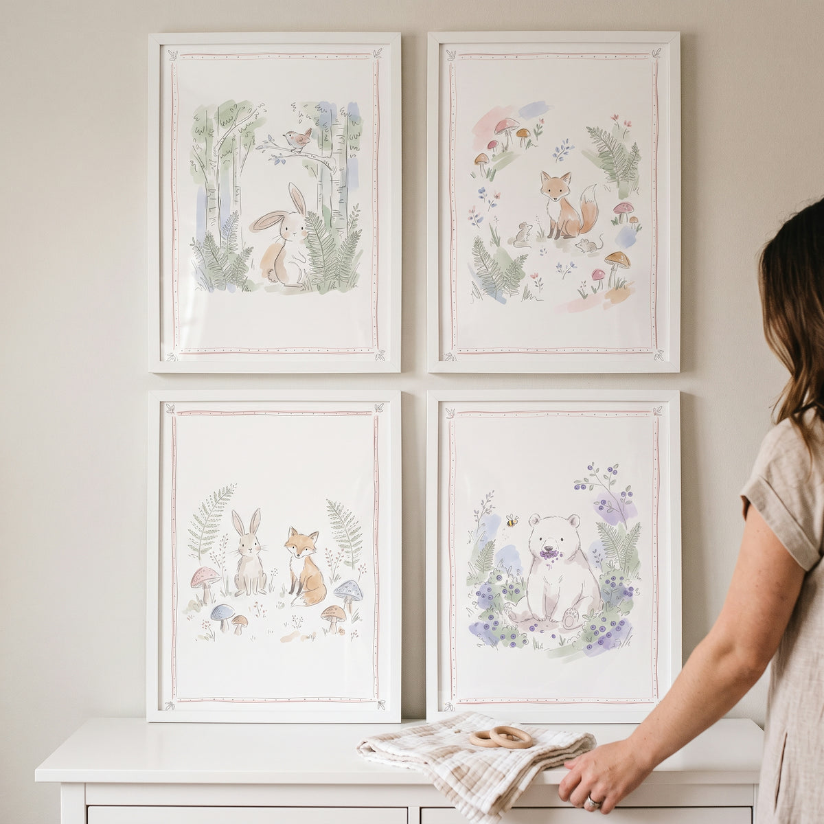 A woman stands by a pale botanical forest animal wall art set of 4 featuring watercolor-style forest animals in white frames.