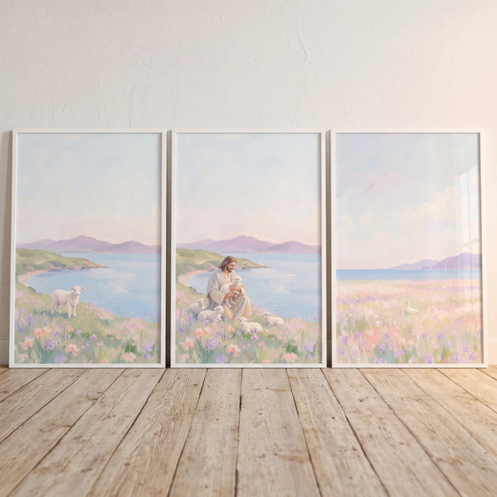Jesus sits with lambs in a pale lilac coastal meadow wall art set of 3 on a light wood floor against a white wall.