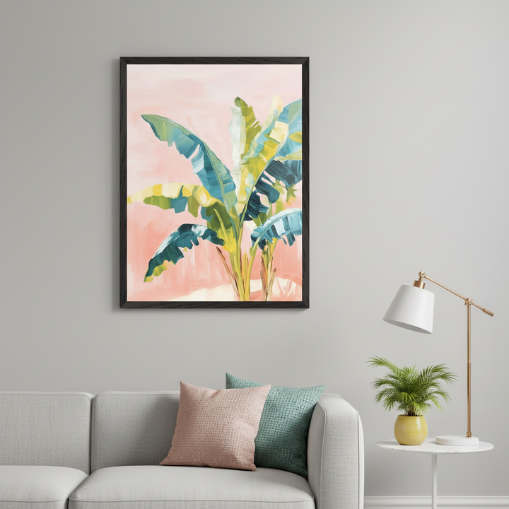 Living room with a light grey sofa. A large framed painting of tropical banana leaves in blue, green, and yellow on a pink background hangs above the sofa. A white side table with a lamp and potted plant is to the right.