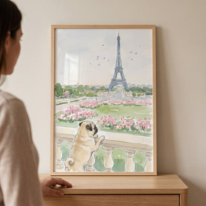 Woman stands by framed paris sightseeing watercolor pug wall art of a pug dog looking at the Eiffel Tower.
