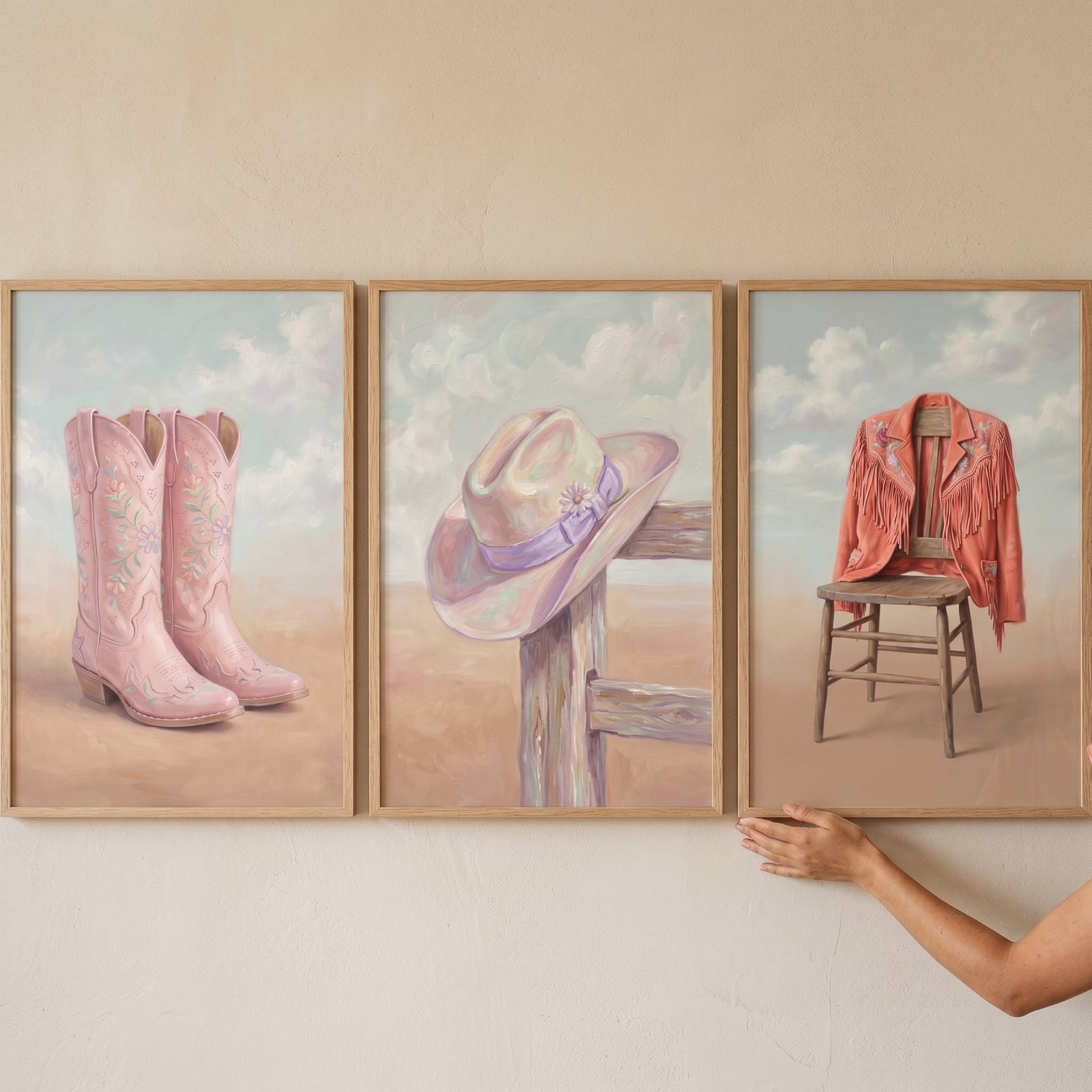 Pastel blush western gear wall art set of 3 with pink boots, a hat on a fence, and a jacket on a wooden chair.