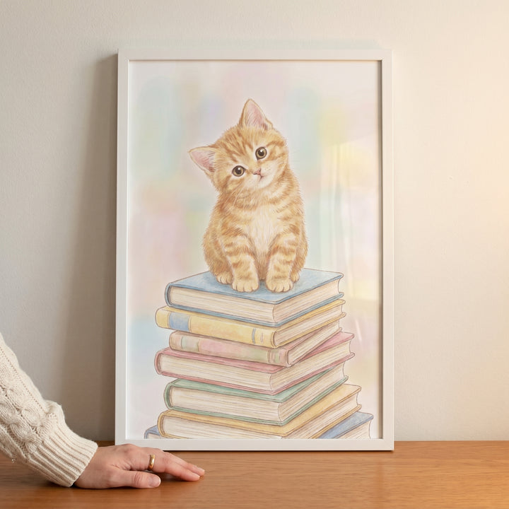 A ginger kitten sits on a colorful stack of books in this framed pastel book stack kitten wall art.