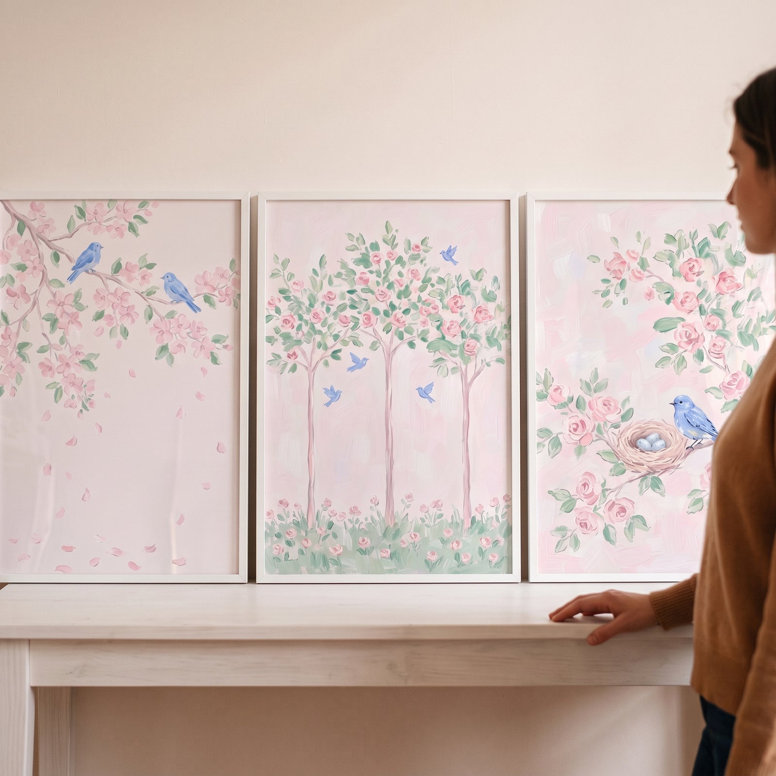 A pastel floral blue bird artwork set of 3 featuring pink flowers and blue birds displayed on a white table.