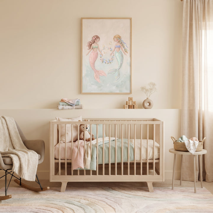Neutral nursery with a wooden crib, rocking chair, and pastel floral wreath mermaid wall art.