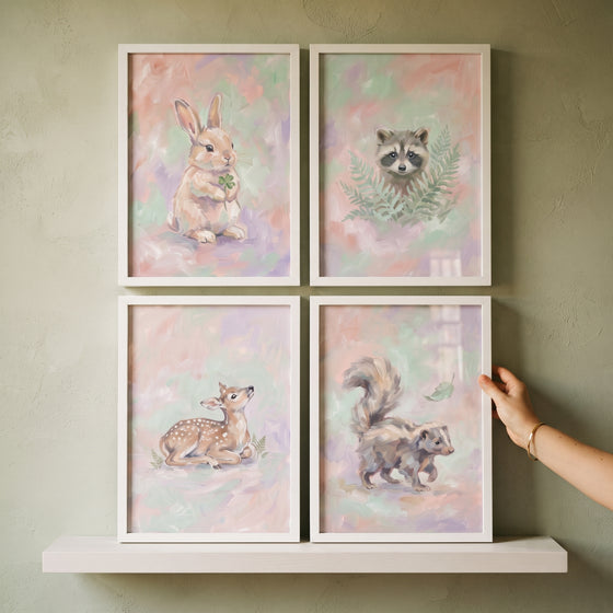 Hand adjusts a pastel meadow woodland animal wall art set of 4 featuring a bunny, raccoon, fawn, and skunk.