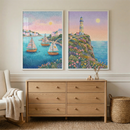 A serene room features two vertical framed art pieces centered above a light oak six-drawer dresser. The left illustration shows three sailboats in a harbor with small cottages under a soft pink sky. The right work features a lighthouse on a cliff covered in wildflowers beside the sea. Both pieces use a fine, dotted texture. The dresser sits on a textured rug next to a cream armchair with a knit throw and a woven storage basket. Soft sunlight fills the peaceful, minimalist space.