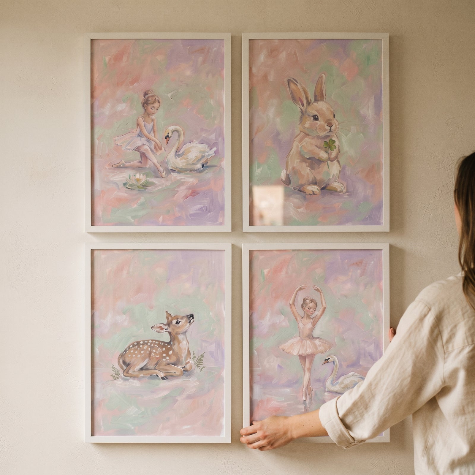 A person hangs a pastel painterly girls room wall art set of 4 featuring a bunny, deer, and ballerinas with swans.