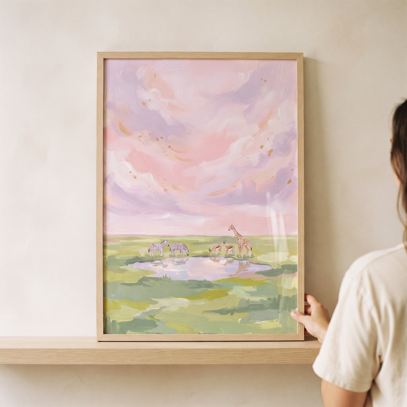Pastel pink savanna animals wall art shows a giraffe, zebras, and gazelles by a waterhole under a soft purple sky.