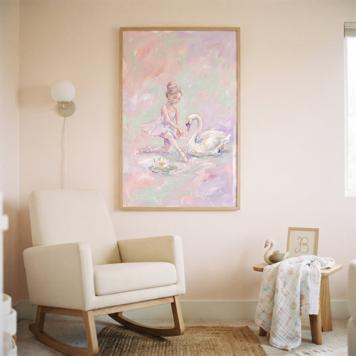 Pastel pink swan ballerina wall art hangs in a wood frame above a cream rocking chair in a soft, neutral nursery.