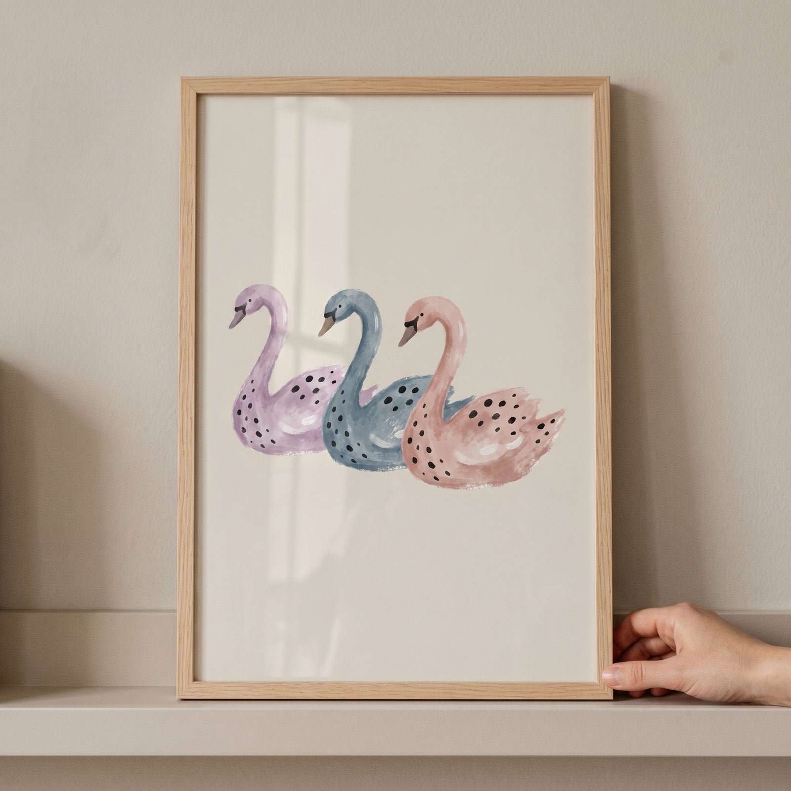 Three purple, blue, and pink swans in a wooden frame. This pastel watercolor spotted swan wall art sits on a shelf.