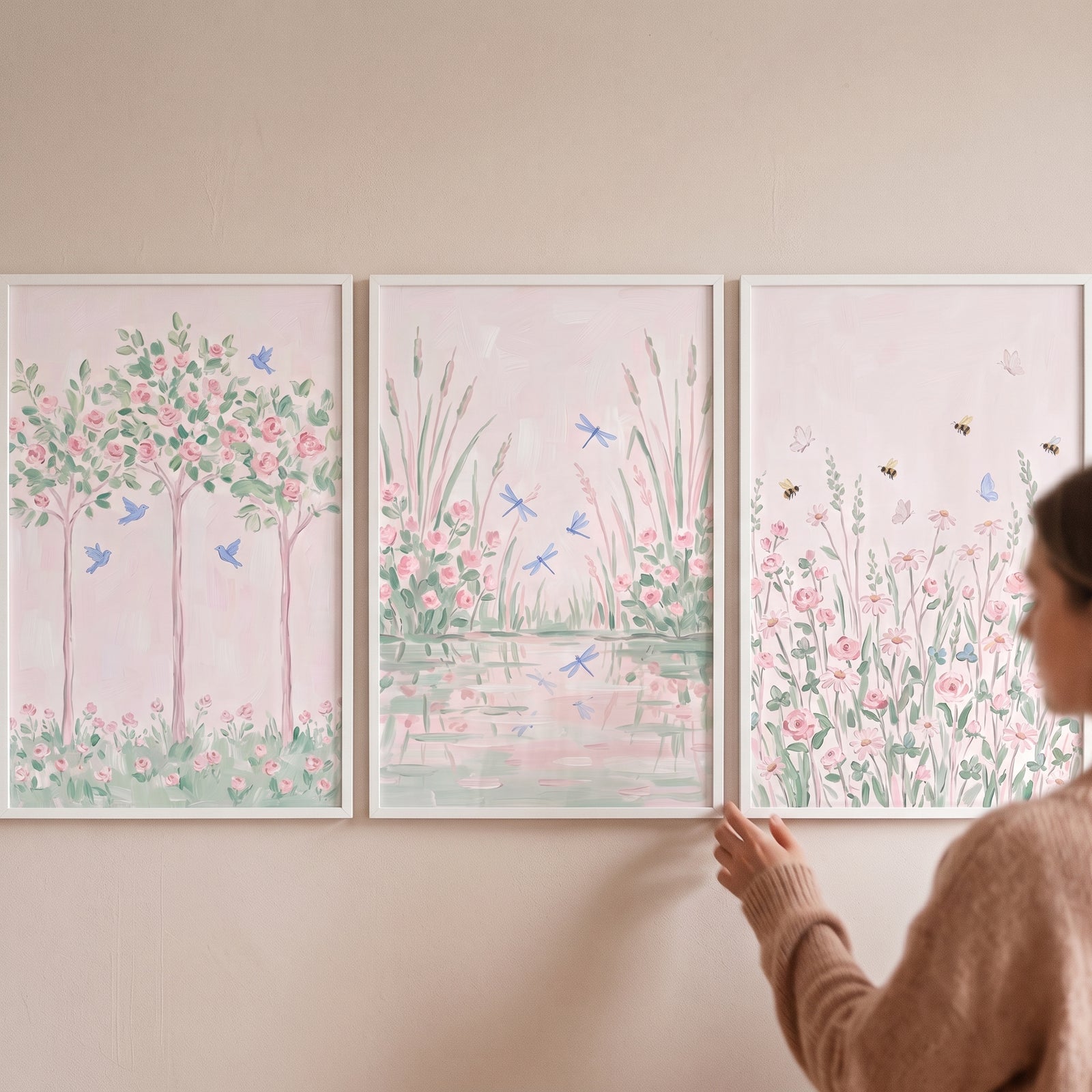 A person adjusts a peaceful pink botanical garden wall art set of 3 featuring birds, dragonflies, and floral scenes.