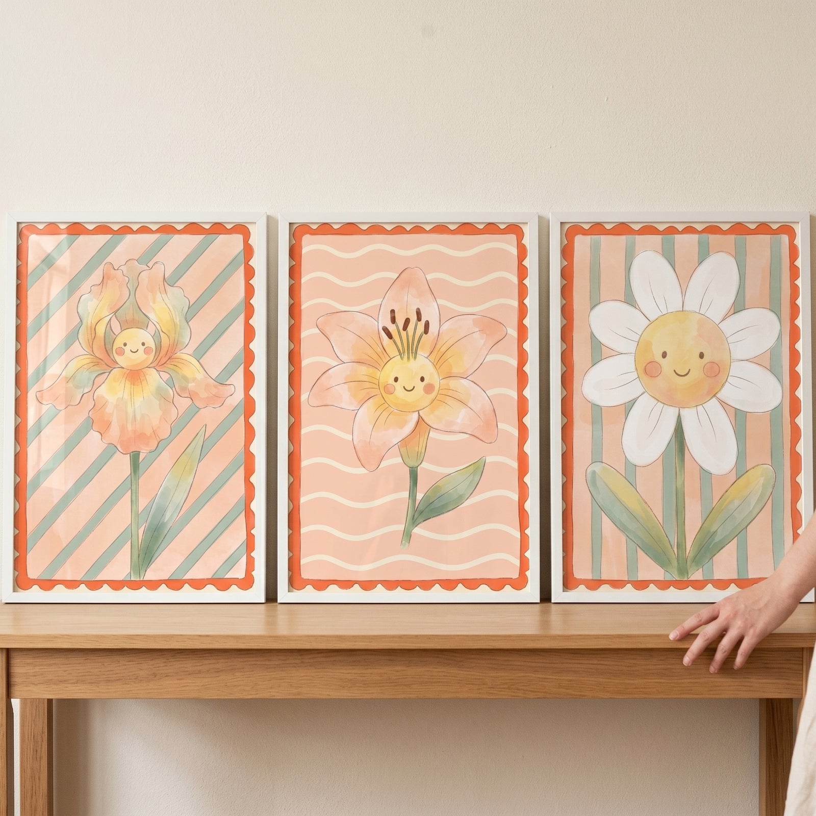 Peach smiling flower wall art set of 3 featuring iris, lily, and daisy characters in white frames on a wooden table.