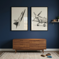 A contemporary interior space features a deep navy blue wall serving as a backdrop for two large, black-framed sketches. The sketch on the left illustrates a sleek modern fighter jet in a dynamic ascending pose, while the one on the right displays a vintage propeller-driven aircraft from a front-quarter perspective. Both pieces are rendered in a detailed, grayscale style on off-white paper.

