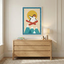 An interior shot of a child's room features a light wood three-drawer dresser against a neutral-colored wall with classic panel molding. Centered above the dresser is a framed graphic print showing a whimsical cartoon penguin wearing orange goggles and snowboarding through the air. The penguin is set against a large yellow sun and flies over three stylized turquoise mountain peaks with white snow caps. The artwork has a blue border with white polka dots. On top of the dresser sits a small stack of colorful