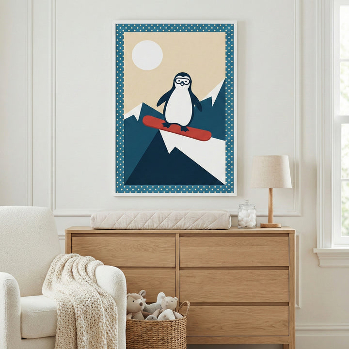 A bright and airy nursery featuring a light wood dresser with a quilted changing pad on top. To the left, a plush white armchair is draped with a chunky knit blanket, and a woven basket filled with stuffed animals sits on the floor nearby. Centered on the wall above the dresser is a framed graphic illustration of a cartoon penguin wearing goggles and snowboarding down a stylized mountain under a pale yellow sky and a large white sun. The artwork has a blue polka-dot border and is encased in a simple white f