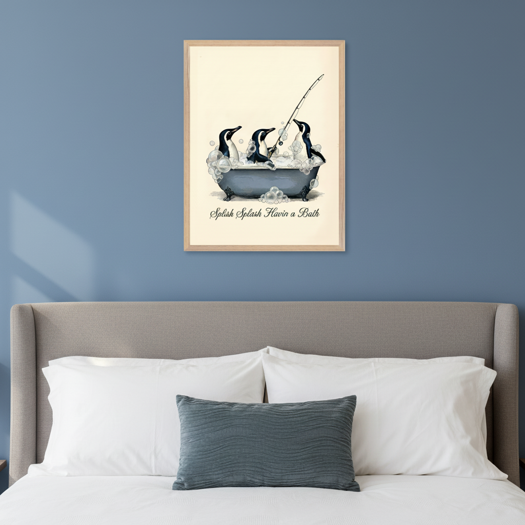 Modern bedroom with a grey upholstered bed. A framed print of three cartoon penguins bathing in a bubble-filled tub, one fishing, hangs centered above the bed. Text reads "Splish Splash Havin a Bath".
