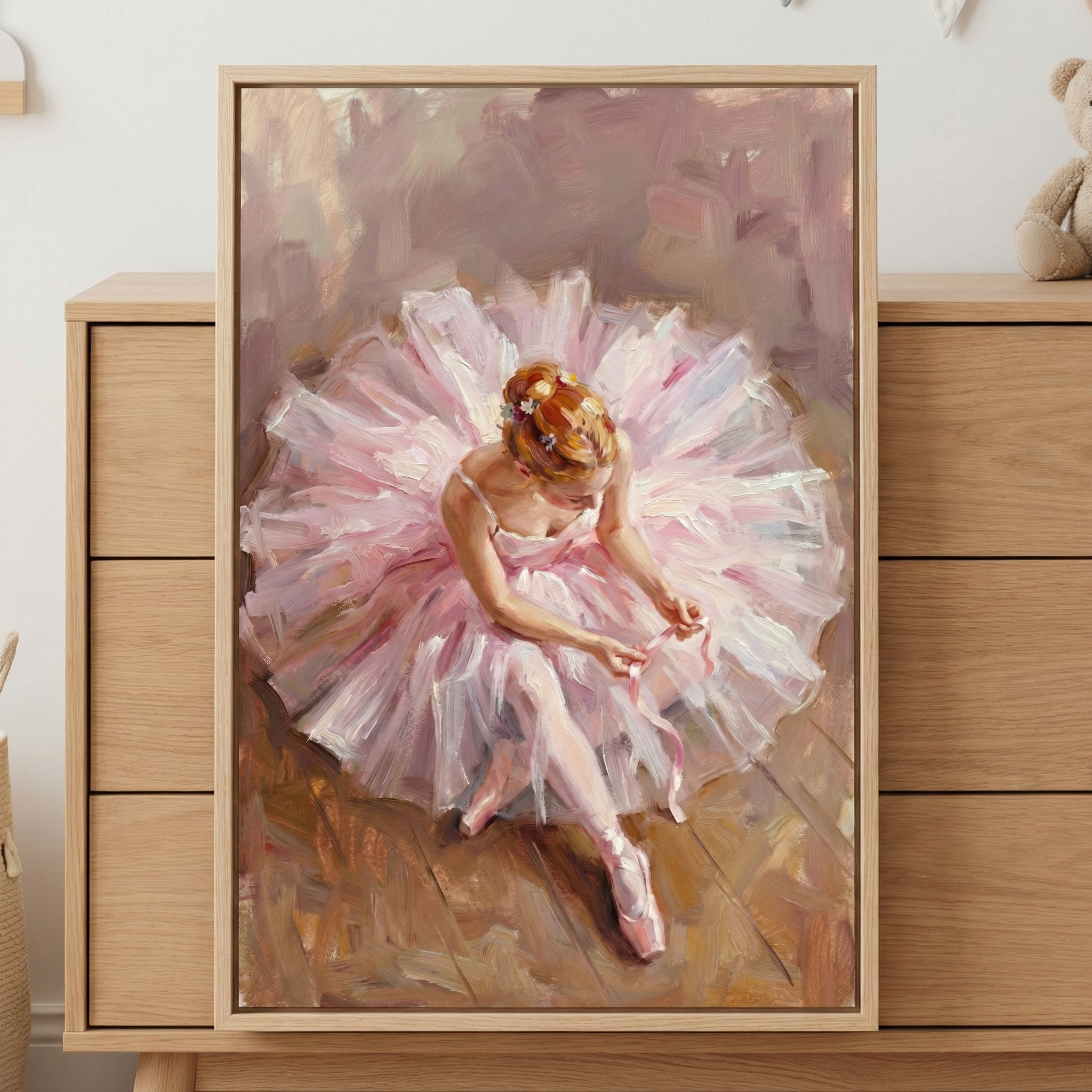 A framed painting of a ballerina in a pink tutu adjusting her ballet shoe ribbons, displayed on a wooden dresser.