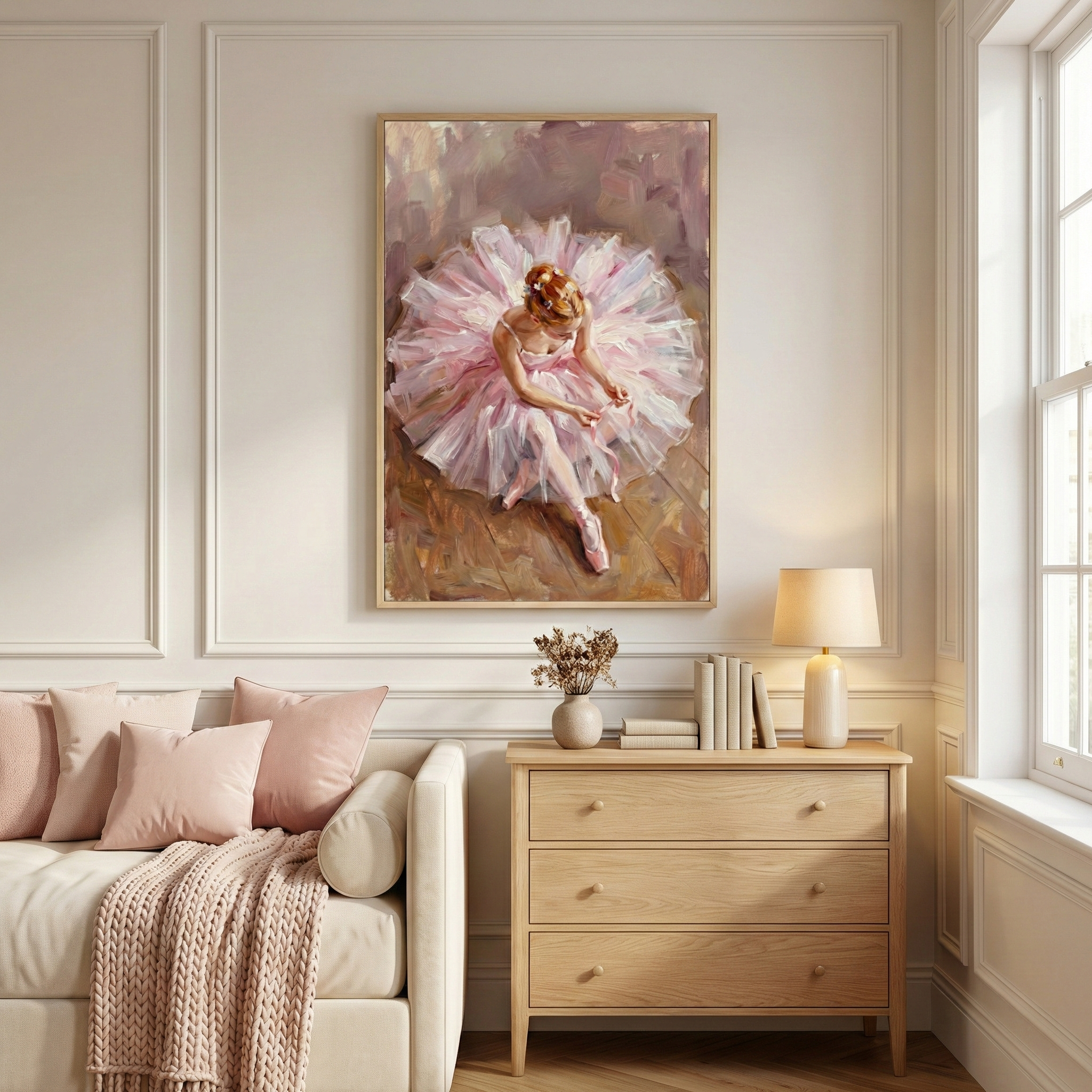 A cozy living room features a painting of a ballerina in a pink tutu, gracefully seated and adjusting her shoes. The artwork hangs above a light wood dresser adorned with books, a vase, and a lamp. A beige sofa with pink cushions and a knitted throw complements the serene atmosphere.