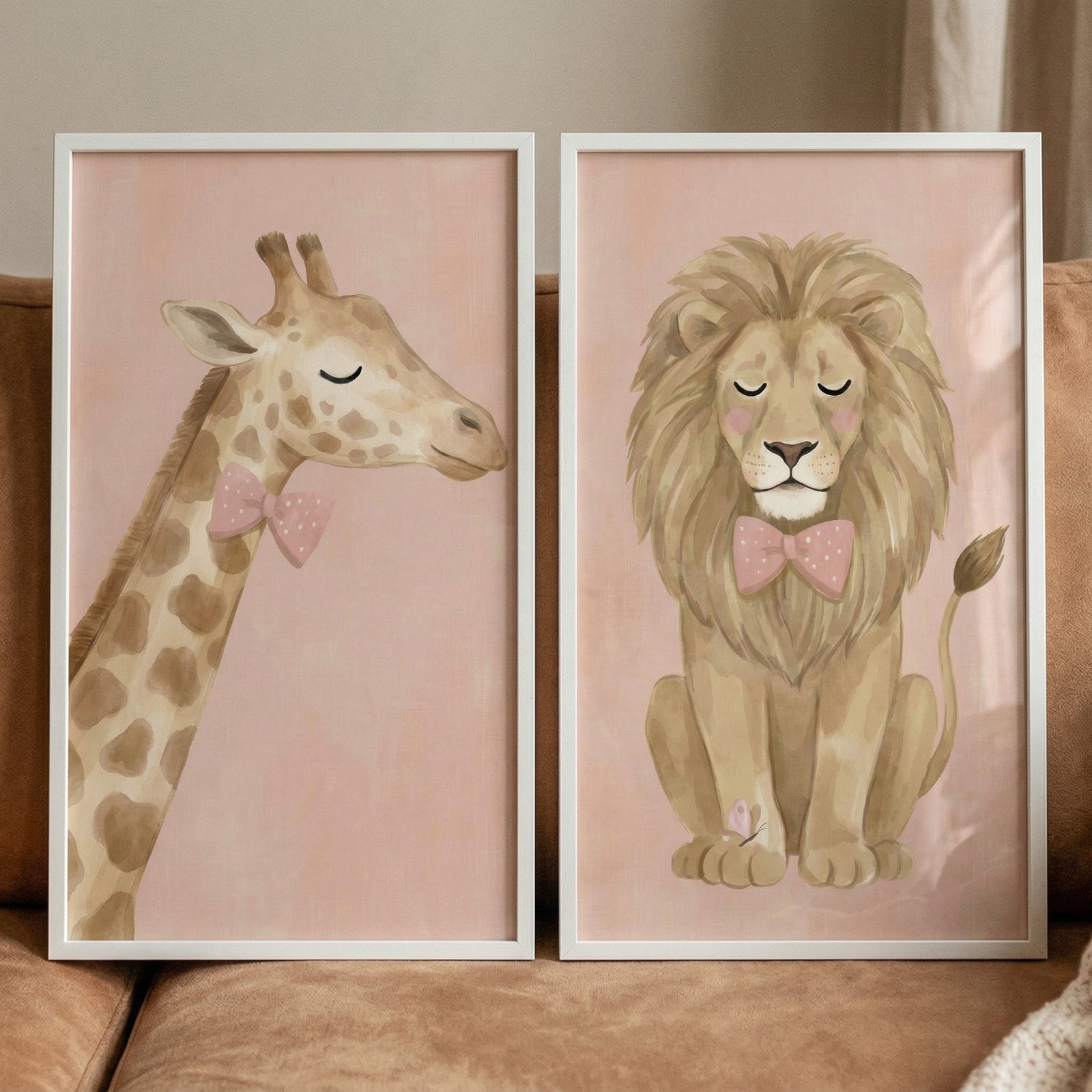 A pair of framed illustrations featuring whimsical animals. On the left, a light brown giraffe with dark spots is shown from the neck up, wearing a soft pink bow tie with tiny white dots. On the right, a seated lion with a thick mane also wears a matching pink bow tie. 